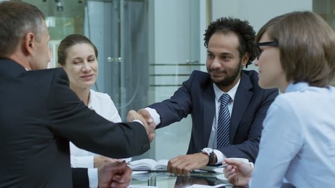 PAN shot of two experienced businessmen shaking hands and speaking with female colleagues at corporate meeting