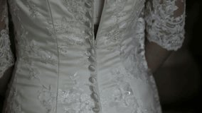 
Close-up of woman hand buttoning the wedding dress. Bridesmaid helps zip up wedding dress.