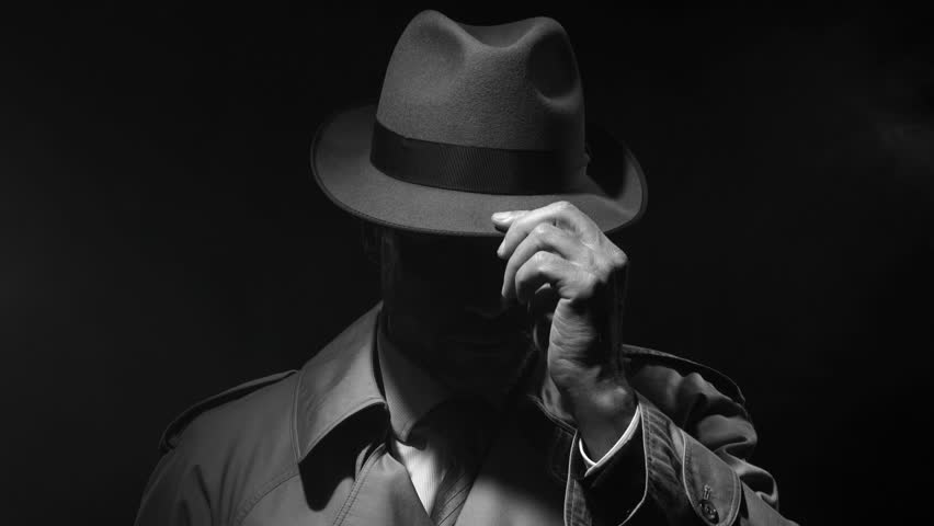 Retro noir film character: confident investigator standing in the dark and adjusting his fedora hat