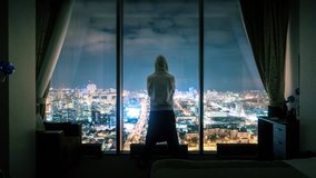 Hooded anonymous man silhouette standing in dark room looking out of panoramic window with illuminated night city view in background. Timelapse, 4K UHD. Zoom in. - Powered by Shutterstock - Get 15% off with code: PIKWIZARD15