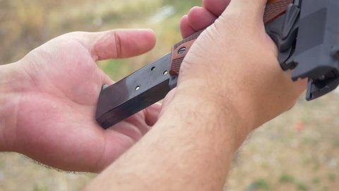 Man loading a handgun in slow motion. Closeup of a male inserting a magazine into a 9mm pistol and pulling the slide releasing a bullet into the chamber representing concealed carry and gun control.