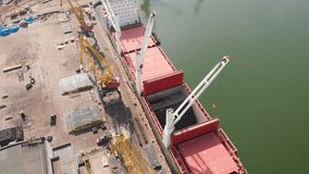 Aerial view of the ship's loading near the berth in the cargo port during the day. Loading of wire rod into ship's hold by ship cranes. Video from the drone 4K.