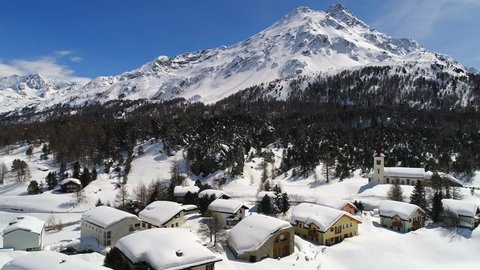 Little village and forest covered with snow. Engadine Valley in the Swiss Alps. Aerial view
