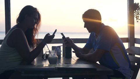 A man and a woman are sitting in a cafe by the sea, everyone is looking into their phone, not a beautiful sunset. slow motion. 1920x1080. full hd