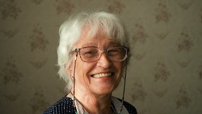 Portrait of a happy grandmother. Happy elderly woman with eyeglasses smiling and looking into a camera. Senior people portrait authentic video. Stay home concept, isolation period for retired people