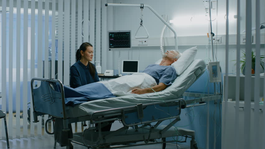 In the Hospital Ward Recovering Father is Visited by Daughter. Senior Sick Man Sleeping in Bed Daughter Sits Beside, Worrying. Modern Private Ward. Family Values. Shot on RED EPIC-W 8K Helium Camera.