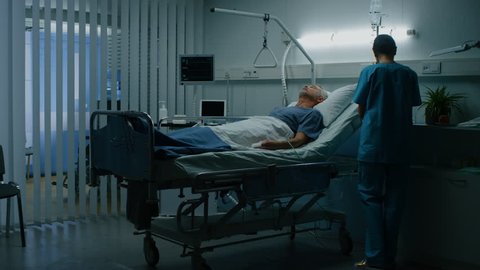 In the Hospital Senior Patient Rests on the Bed, Nurse Enters Ward and Does Checkup. Recovering Man Sleeping in the Modern Hospital Ward. Shot on RED EPIC-W 8K Helium Cinema Camera.