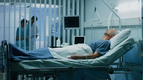 In the Hospital Sick Man Rests, Lying on the Bed. Recovering Man Sleeping in the Modern Hospital Ward. Shot on RED EPIC-W 8K Helium Cinema Camera.