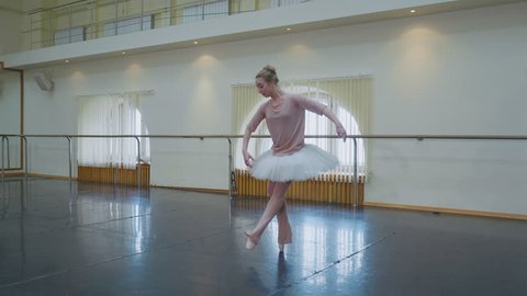 Ballerina in white ballet tutu dress practicing in dance studio or gym. Woman jumping in class room. Alone warming up before performance. Amazing dance. 4k Video Stok