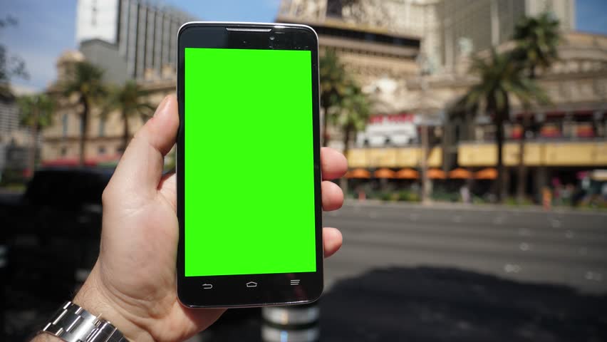 A man holds his smartphone outside the Paris Hotel and Eiffel Tower in Las Vegas. Green screen with optional corner pin markers for advanced screen replacement. Shot at 60fps.  	