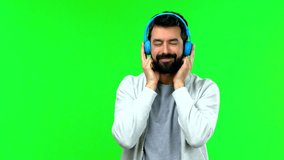 Handsome man with beard listening to music with headphones on green screen chroma key
