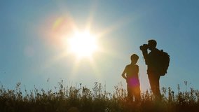 Family of father and son walk along grassy hill using old vintage camera for filming video. Little kid's and adult man's male silhouettes isolated at bright blue sky and sunshine background. 