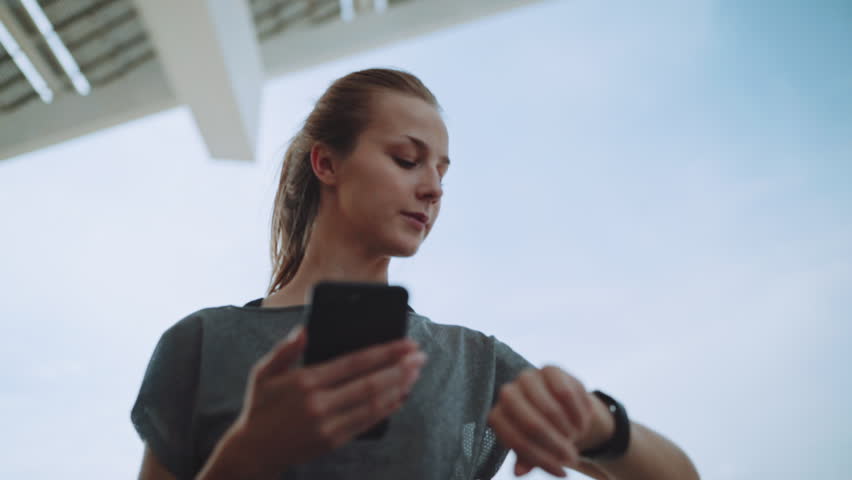 Pretty smiling fitness woman using running app before the run for track the pace on smartwatch, happy smiling sportive girl texting message on smartphone before morning workout, Slow Motion Royalty-Free Stock Footage #1009742309