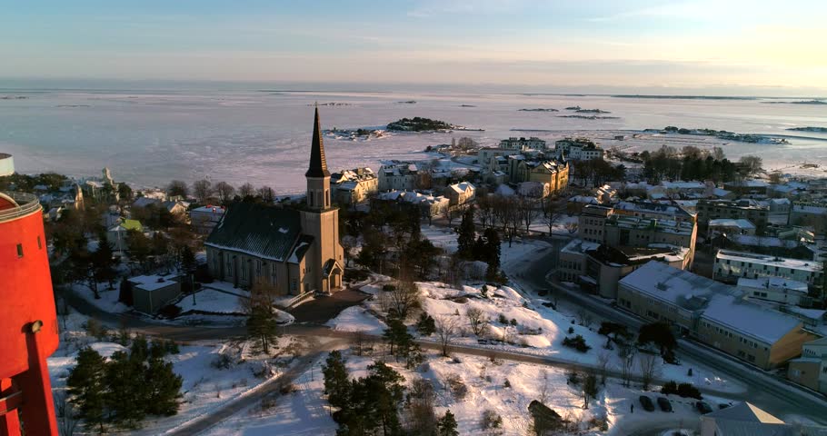 Frozen city, Cinema 4k aerial view around a water tower and revealing a church, in a icy Hanko cityscape, on a cold sunny winter evening dawn, in Uusimaa, Finland
