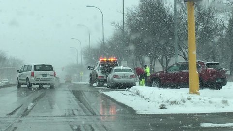 Snow storm with tow truck driver helping stranded driver on busy street. 