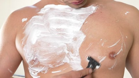 The naked man shaves his chest. A man with white foam for shaving on his chest. Men's shave body with foam and razor. 4k
