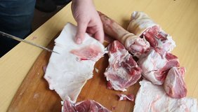 Man holding knife with hands, cutting, chopping, preparing pig  raw, fresh meat steak for barbecue. Close up video footage of butcher cutting raw red bbq meat on cutting board.
