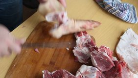 Man holding knife with hands, cutting, chopping, preparing pig  raw, fresh meat steak for barbecue. Close up video footage of butcher cutting raw red bbq meat on cutting board.