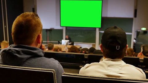 Professor or teacher delivers a lecture college to a large audience of students with greenscreen beamer background 