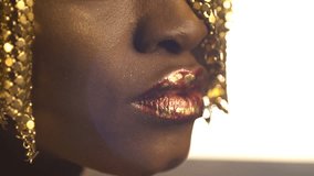 Open and closed eyes with bronze eyeshadows and cat eyes on the face of african girl wearing golden jewellery on her head. Close-up view.