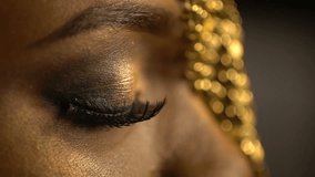 Female blinking eye of the african woman covered with golden eyeshadows and eyeliner. Close-up view. Make-up and fashion concept.