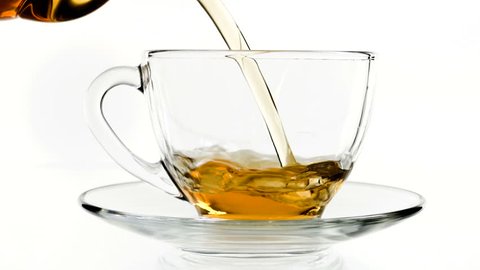 Tea pouring. Tea being poured into glass transparent tea cup. Tea time. Transparent glass teapot and teacup. Slow motion