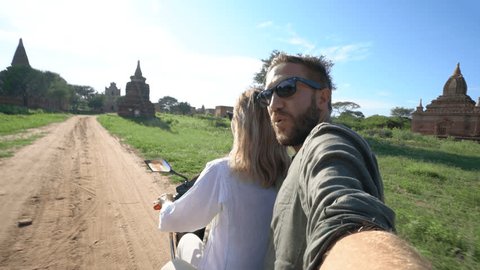 Young couple on a electric bike in Asia take selfies. Couple travelling exploring ancient temple area in Myanmar taking selfies on the go. Adventure selfies point of view 