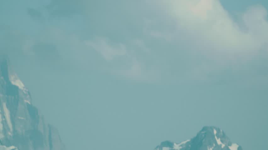 Orange metal drum tourist shelter with green biotoilet at hight rocky mountain peaks covered in snow picturesque landscape on sunny day with blue sky, tracking shot