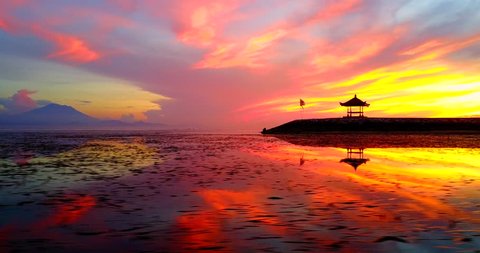 Traversing View Asian Pagoda On Ocean Coast During Tropical Sunrise With Water Reflecting Orange, Red And Yellow Sunlight - Sanur Beach, Indonesia
