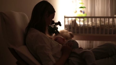 Young beautiful mother, breastfeeding her newborn baby boy at night, dim light. Mom breastfeeding infant
