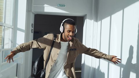 Cool african american guy dancing listening to music in headphones walking and passing by group of classmates making thumbs up to him. Translation of green sign means Exit