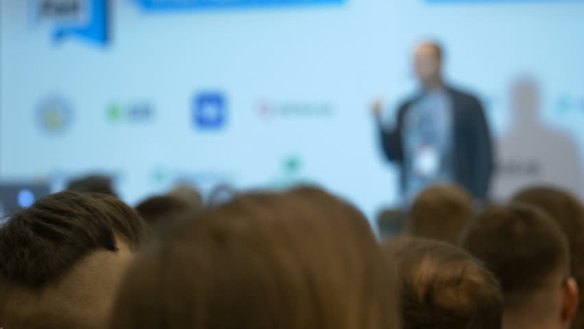 Blurred professional confident manager speaking at symposium for the public of male female persons, answering for colleagues from the big finance companies, giving advices, showing concept at chart