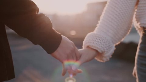 Slow motion soft focus tender and sensual, moving shot of couple holding hands and caressing each other fingers on sunset filled beautiful evening at terrace or rooftop, concept love and relationship
