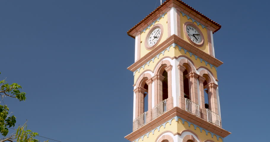 Establishing shot of the clock tower of the Parroquia de la Santa Cruz in Puerto Vallarta, Mexico against a clear blue sky