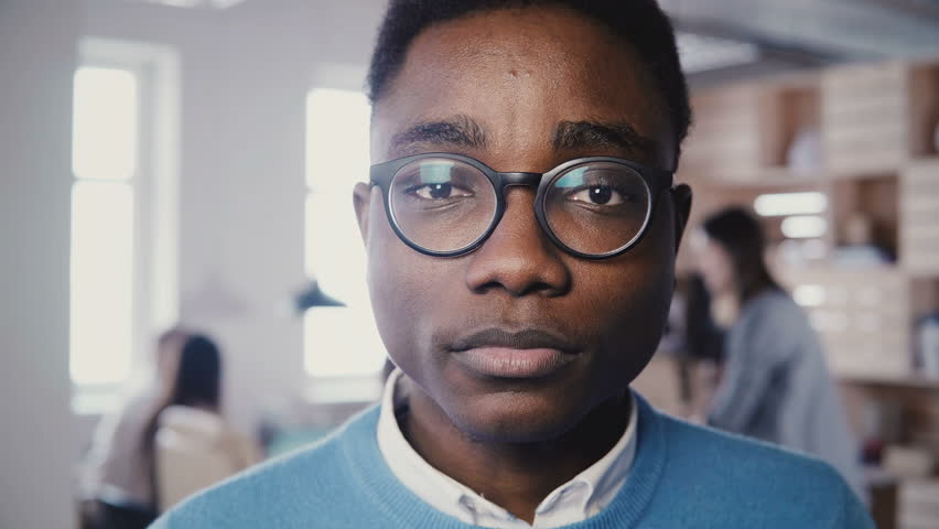 Incredible close-up portrait of handsome young African American man in glasses smiling at camera in busy office 4K. | Shutterstock HD Video #1009818323