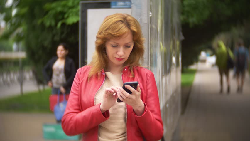 woman standing at the bus stop and using a cellphone. 4k