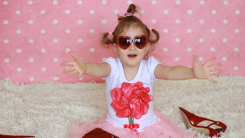 Sweet little girl in red sunglasses in the shape of hearts sends air kisses. Funny child send kiss. Pink background. Fashionista. Heart. Love