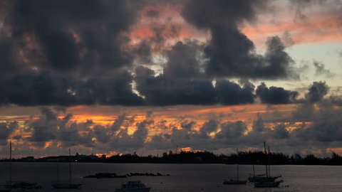 Sun sets on a bay in Bermuda, with big clouds moving.