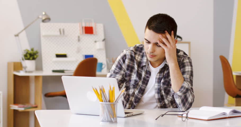 Tired young caucasian man working on the laptop computer in the modern ofice, then lying his head on the table and sleeping. Inside