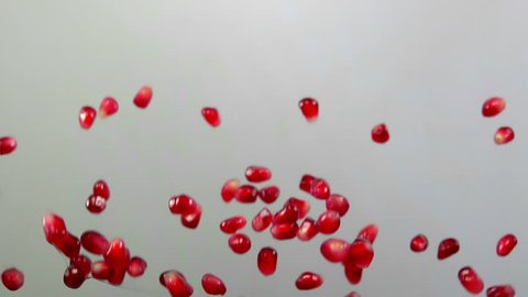 Red ripe garnet seeds bouncing against to the camera on a white background in slow motion