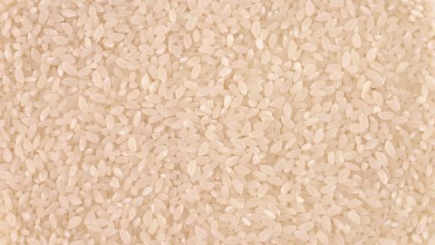 Full frame background of raw white rice rotating on turn table. Loopable. Close up macro. View from above/overhead.