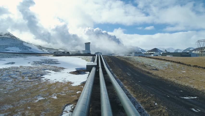 Slow Motion: Pipes leading to Geothermal Power Plant. Steam are generated in the background. Snowy environment 