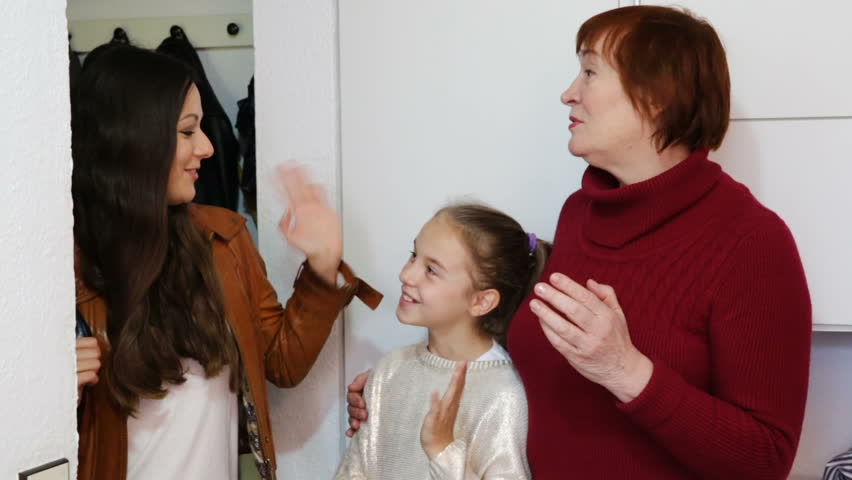 Happy young mother leaving daughter with grandma at home, saying goodbye