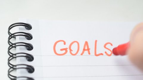 Hand writing the word GOALS with red marker in spiral notepad, business concept
