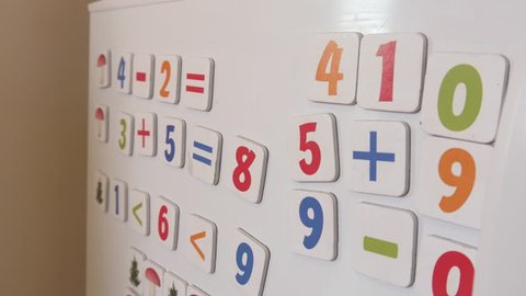 WROCLAW, POLAND - APRILE 01, 2018: Kid plays with Magnets of simple Mathematical Numbers on a Refrigerator
