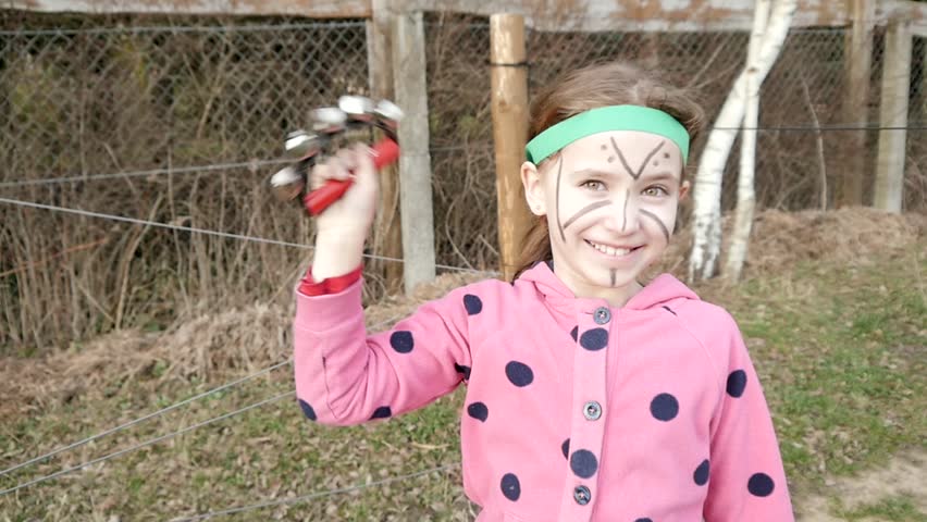 Happy smiling Girl with painted Face Mask playing Tambourine in Indian Camp