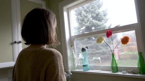 Woman with depression, sadness, loneliness or abuse, etc. staring out the window from her kitchen reveal.