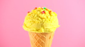 Ice cream cone close-up. Icecream scoop in waffle cone rotated on pink color background.  Banana, vanilla or lemon flavor sweet dessert closeup, rotation. 4K UHD