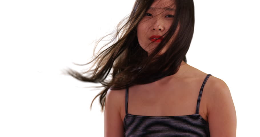 Portrait of cute millennial woman looking at camera with hair blowing for copyspace. Lovely Asian female posed for camera with hair blowing in face isolated on white background. 4k
