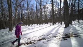 Wide tracking clip of pretty, mature woman hiking in a snowy forest on a sunny winter day.